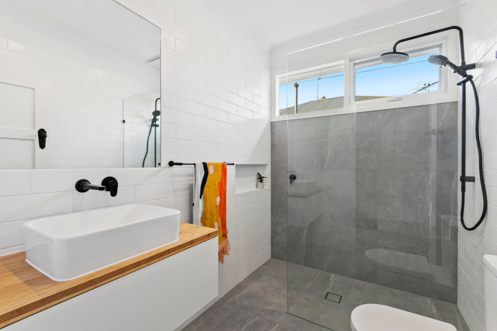 Inspiration for a mid-sized contemporary bathroom in Geelong with white walls, wood benchtops, flat-panel cabinets, white cabinets, a curbless shower, gray tile, a vessel sink, grey floor and brown benchtops.