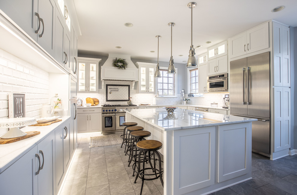 This is an example of a transitional kitchen in DC Metro with an undermount sink, shaker cabinets, white cabinets, white splashback, subway tile splashback, stainless steel appliances, with island, grey floor and white benchtop.