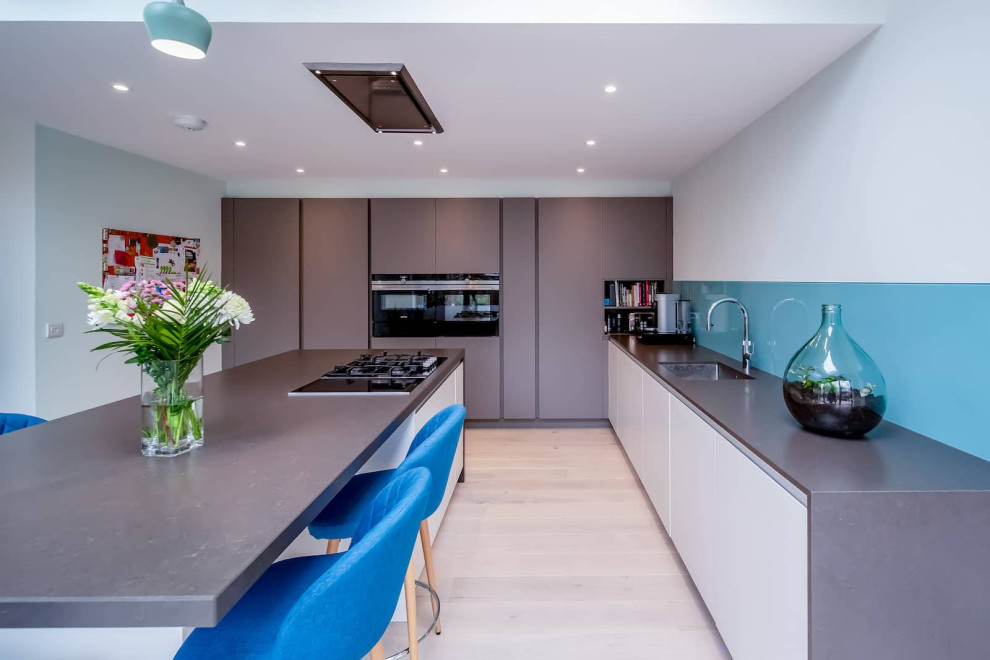 Design ideas for a large contemporary l-shaped open plan kitchen in London with a single-bowl sink, flat-panel cabinets, grey cabinets, quartzite benchtops, blue splashback, black appliances, light hardwood floors, with island, beige floor and grey benchtop.