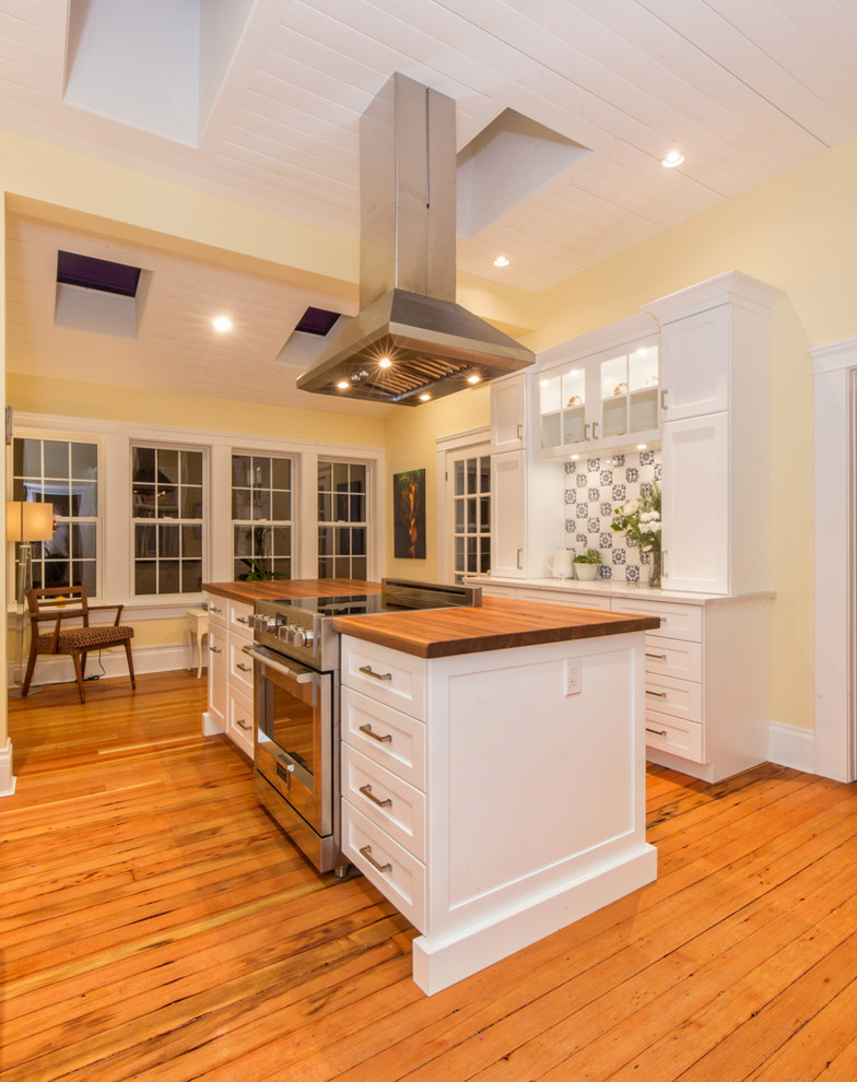 This is an example of a large country galley kitchen pantry in Other with a farmhouse sink, shaker cabinets, white cabinets, wood benchtops, white splashback, mosaic tile splashback, stainless steel appliances, medium hardwood floors, with island and orange floor.