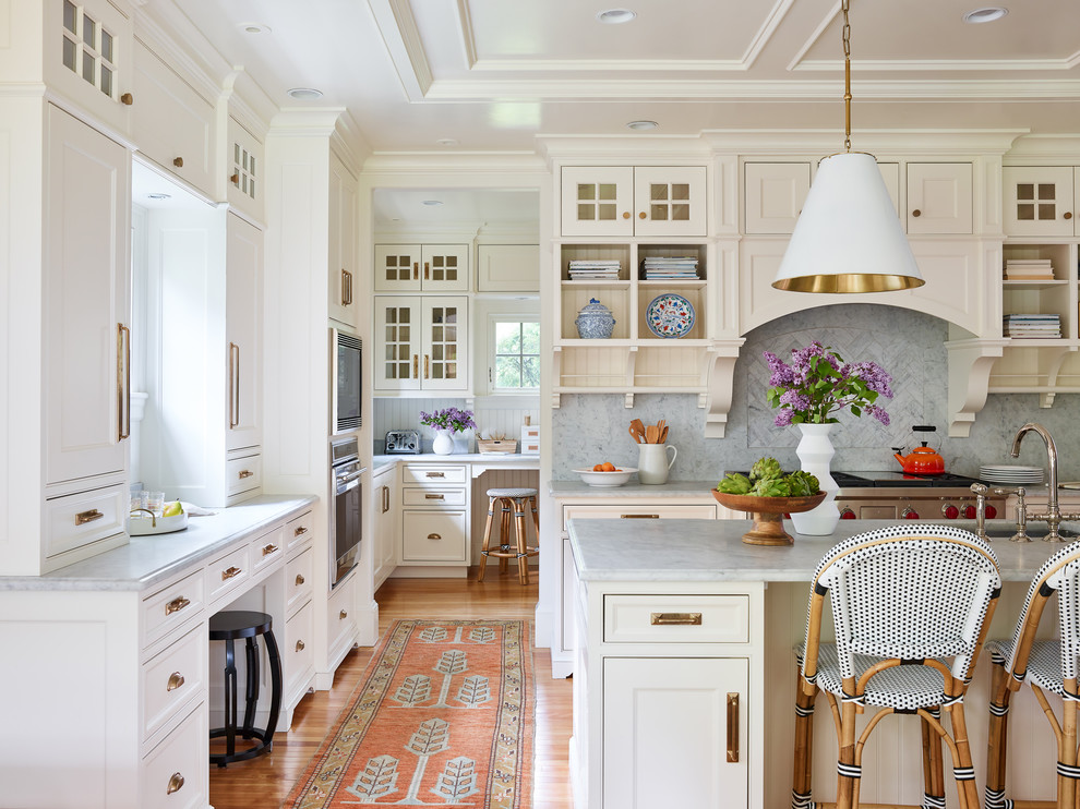 Photo of a large traditional l-shaped eat-in kitchen in Boston with an undermount sink, beaded inset cabinets, white cabinets, marble benchtops, white splashback, marble splashback, panelled appliances, medium hardwood floors, with island, brown floor and grey benchtop.