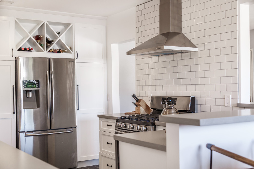 Inspiration for a mid-sized contemporary u-shaped separate kitchen in Orange County with a farmhouse sink, shaker cabinets, white cabinets, concrete benchtops, white splashback, subway tile splashback, stainless steel appliances, laminate floors, a peninsula, black floor and grey benchtop.