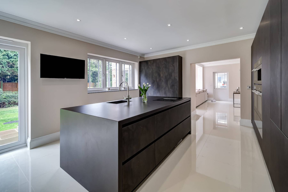 This is an example of a large modern galley open plan kitchen in London with a built-in sink, flat-panel cabinets, dark wood cabinets, black appliances, porcelain flooring, multiple islands, white floors and black worktops.