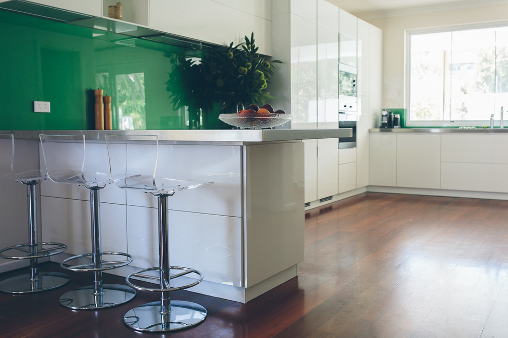 Inspiration for a large contemporary eat-in kitchen in Perth with a double-bowl sink, white cabinets, stainless steel benchtops, metallic splashback, glass sheet splashback, stainless steel appliances and medium hardwood floors.