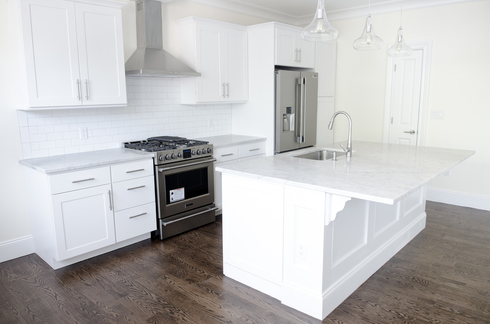 This is an example of a large transitional single-wall kitchen in New York with an undermount sink, shaker cabinets, white cabinets, quartz benchtops, white splashback, subway tile splashback, stainless steel appliances, dark hardwood floors, with island and brown floor.