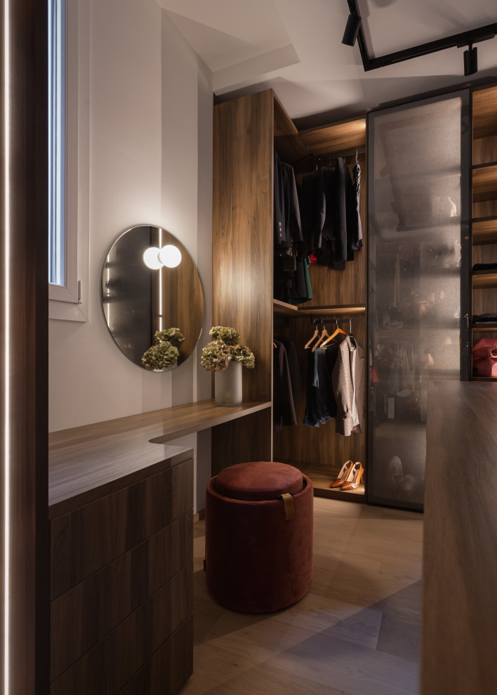 This is an example of a large contemporary gender-neutral walk-in wardrobe in Milan with glass-front cabinets, dark wood cabinets, painted wood floors and beige floor.