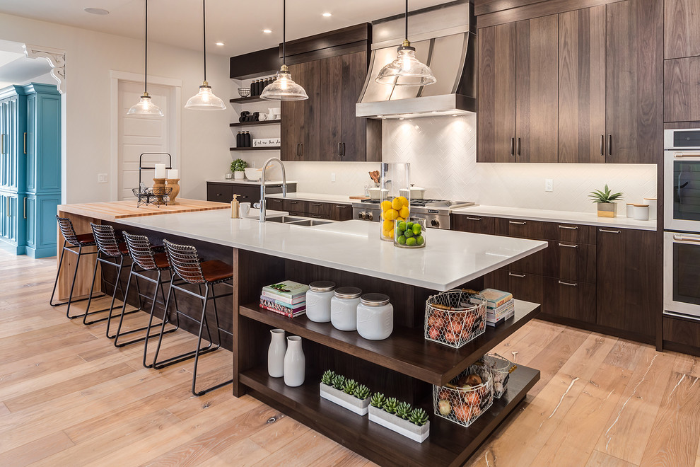 This is an example of a large country kitchen in Calgary with flat-panel cabinets, dark wood cabinets, quartz benchtops, white splashback, subway tile splashback, stainless steel appliances, light hardwood floors, with island, beige floor and a farmhouse sink.