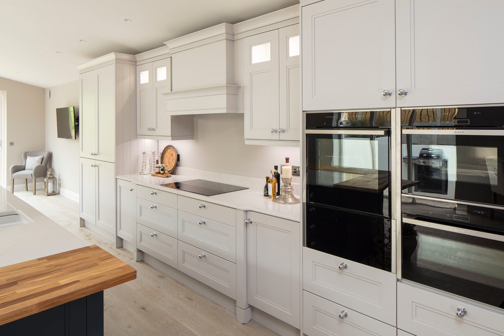 Photo of a country open plan kitchen in Dublin with with island, recessed-panel cabinets, white cabinets and wood benchtops.