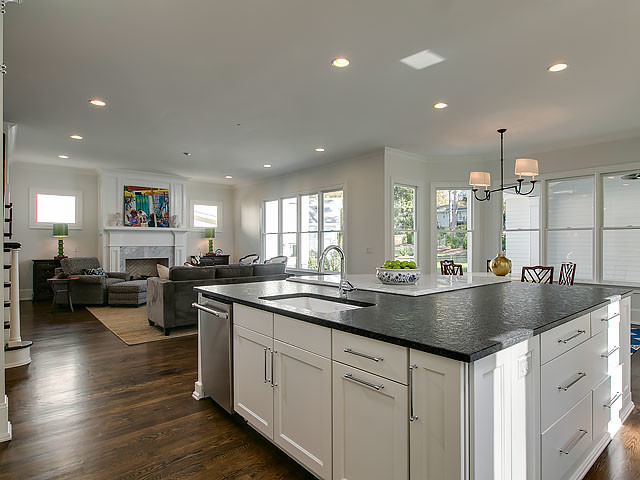 Large transitional l-shaped open plan kitchen in Raleigh with an undermount sink, recessed-panel cabinets, white cabinets, solid surface benchtops, white splashback, glass tile splashback, stainless steel appliances, medium hardwood floors, with island, brown floor and white benchtop.