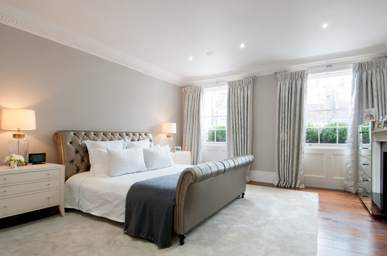 Inspiration for a large transitional master bedroom in London with grey walls, medium hardwood floors, a standard fireplace, a stone fireplace surround and brown floor.