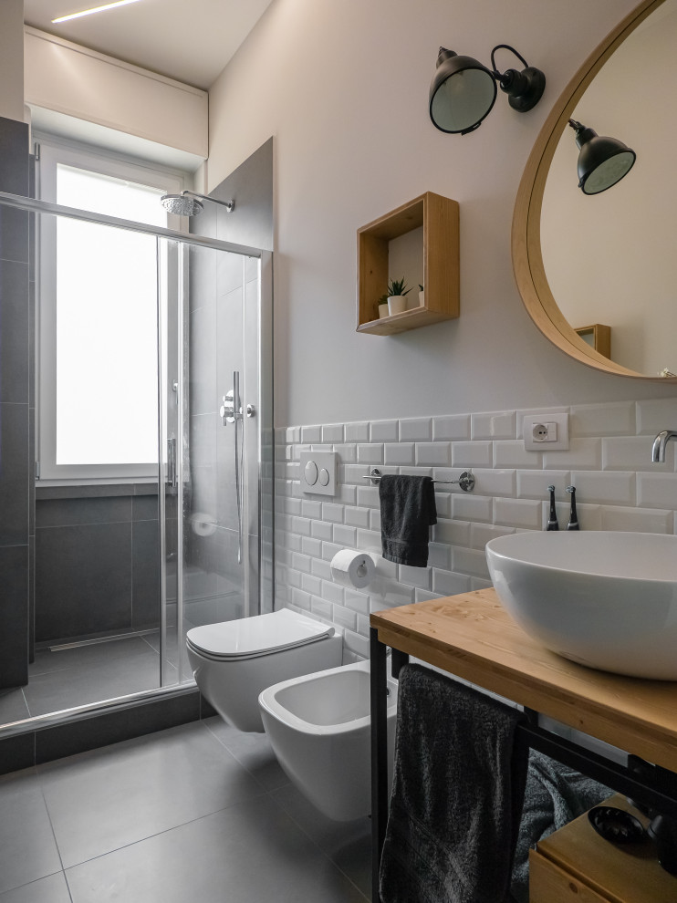 Photo of a medium sized urban shower room bathroom in Milan with open cabinets, light wood cabinets, an alcove shower, a two-piece toilet, white tiles, porcelain tiles, grey walls, porcelain flooring, a vessel sink, wooden worktops, grey floors, a sliding door, a single sink, a freestanding vanity unit and a drop ceiling.
