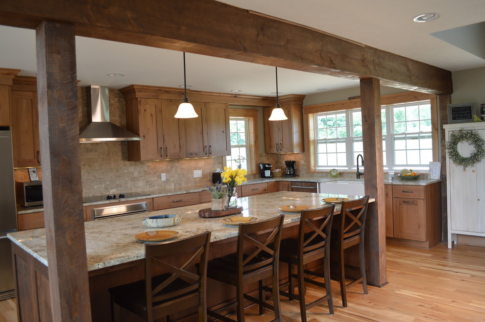 Design ideas for an expansive country l-shaped open plan kitchen in Cleveland with a farmhouse sink, shaker cabinets, medium wood cabinets, granite benchtops, beige splashback, stone tile splashback, stainless steel appliances, light hardwood floors and with island.