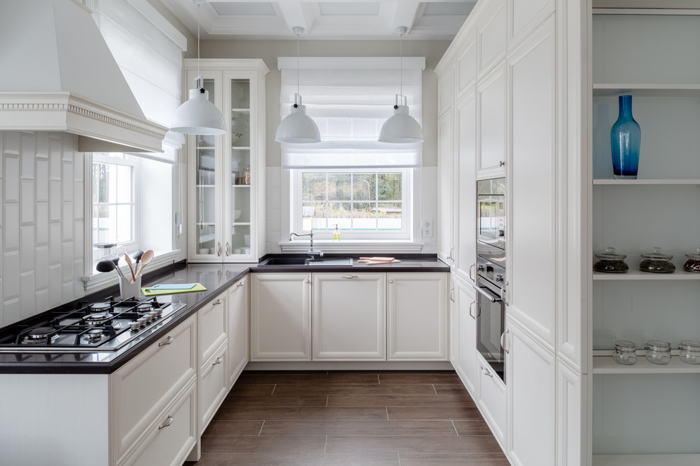 Inspiration for a traditional u-shaped kitchen in Moscow with recessed-panel cabinets, white cabinets, white splashback, stainless steel appliances, dark hardwood floors, no island, brown floor and window splashback.