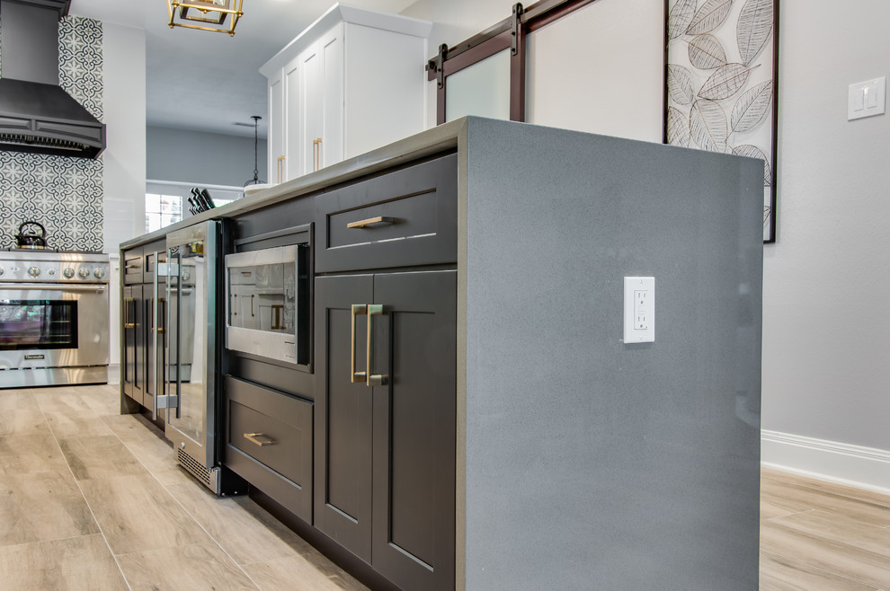 Inspiration for a large transitional l-shaped porcelain tile and gray floor kitchen pantry remodel in Houston with a farmhouse sink, shaker cabinets, white cabinets, quartzite countertops, white backsplash, glass tile backsplash, stainless steel appliances, an island and white countertops