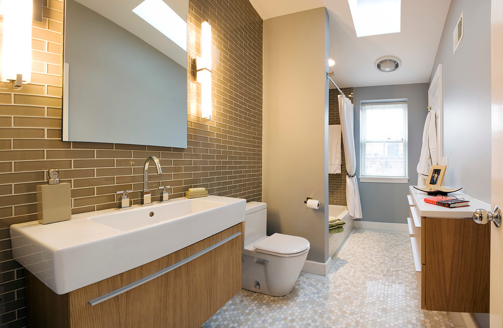 Mid-sized contemporary master bathroom in Boston with flat-panel cabinets, medium wood cabinets, an alcove tub, a shower/bathtub combo, a one-piece toilet, brown tile, glass tile, grey walls, marble floors, an integrated sink, a shower curtain and white benchtops.