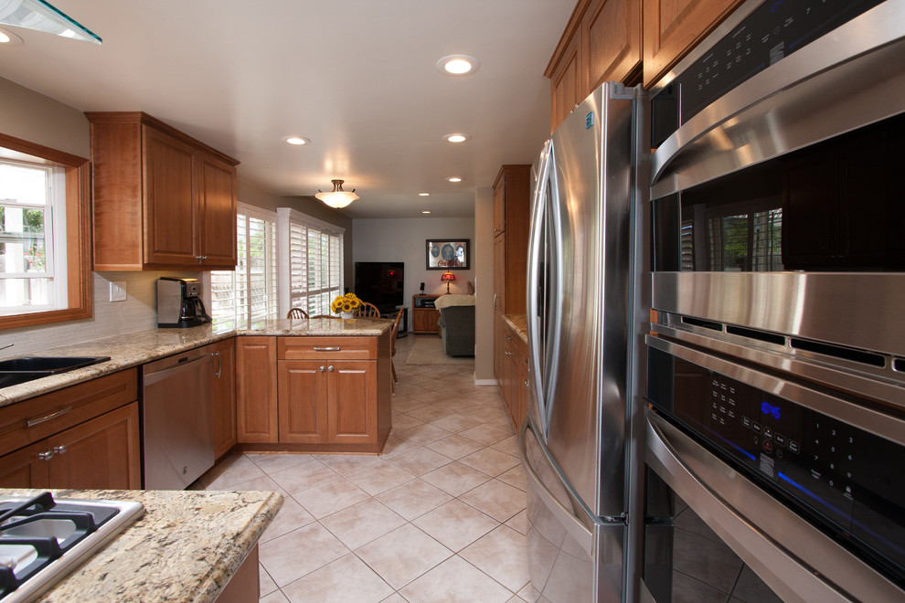 Inspiration for a mid-sized transitional u-shaped ceramic tile kitchen remodel in San Diego with a double-bowl sink, raised-panel cabinets, medium tone wood cabinets, solid surface countertops, white backsplash, ceramic backsplash, stainless steel appliances and a peninsula