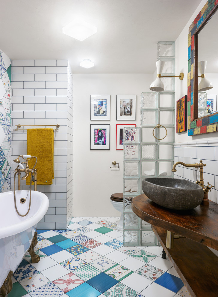 This is an example of an eclectic master bathroom in Moscow with open cabinets, a claw-foot tub, white tile, white walls, a vessel sink, multi-coloured floor, a shower/bathtub combo, a two-piece toilet, subway tile, ceramic floors, wood benchtops and brown benchtops.