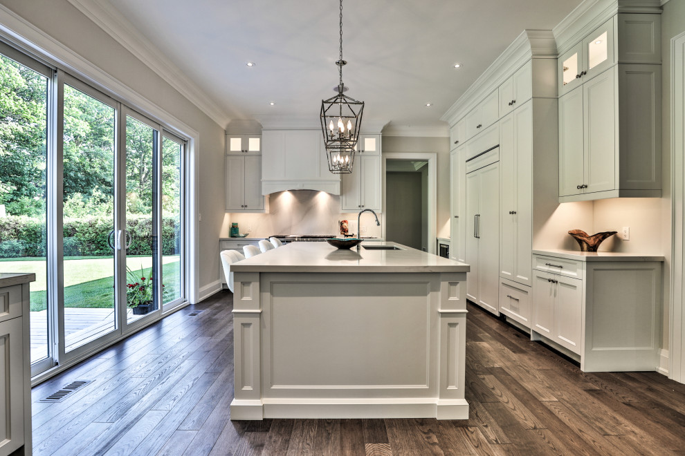 Inspiration for a large transitional l-shaped open plan kitchen in Toronto with an undermount sink, recessed-panel cabinets, white cabinets, panelled appliances, medium hardwood floors, with island, brown floor, white splashback, quartz benchtops, white benchtop and stone slab splashback.