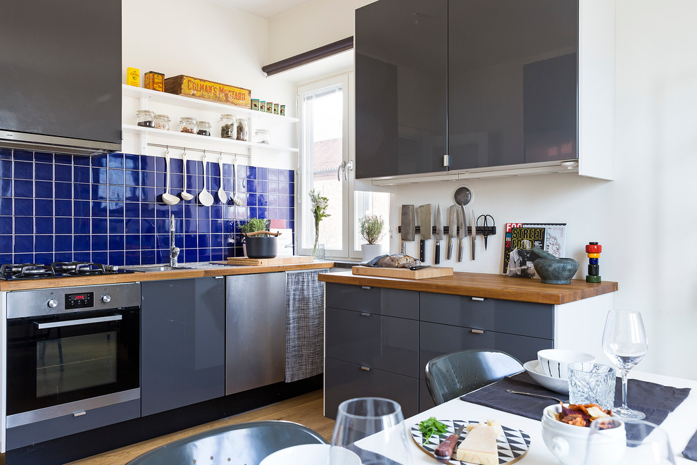 This is an example of a mid-sized scandinavian l-shaped eat-in kitchen in Stockholm with flat-panel cabinets, grey cabinets, wood benchtops, blue splashback, stainless steel appliances and no island.