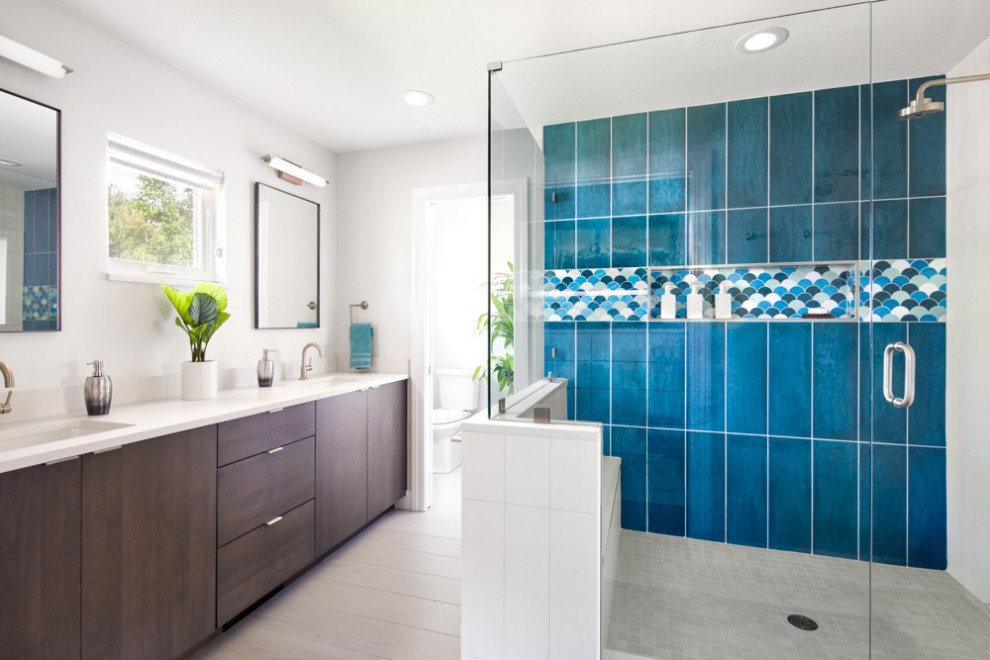 This is an example of a mid-sized contemporary master wet room bathroom in Denver with flat-panel cabinets, dark wood cabinets, a one-piece toilet, blue tile, ceramic tile, white walls, a drop-in sink, granite benchtops, a hinged shower door and white benchtops.