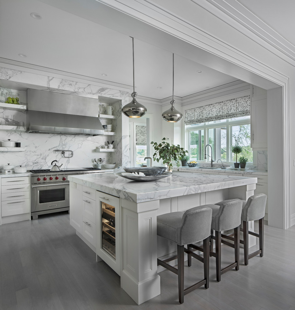 Photo of a transitional l-shaped kitchen in Detroit with recessed-panel cabinets, white cabinets, grey splashback, stainless steel appliances, with island, grey floor and grey benchtop.