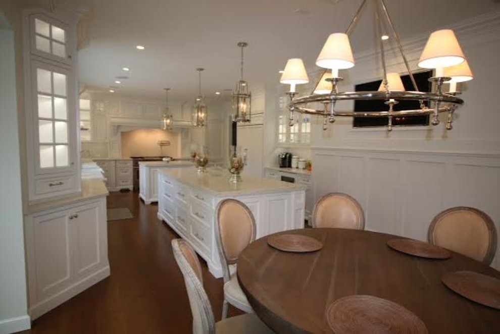 This is an example of an expansive contemporary u-shaped eat-in kitchen in Orange County with a farmhouse sink, shaker cabinets, white cabinets, marble benchtops, white splashback, white appliances, medium hardwood floors, multiple islands and brown floor.