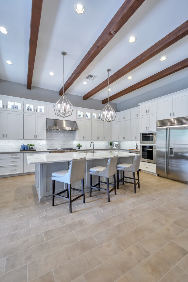 Inspiration for a large transitional l-shaped porcelain tile and brown floor eat-in kitchen remodel in Phoenix with a farmhouse sink, shaker cabinets, white cabinets, quartz countertops, white backsplash, subway tile backsplash, stainless steel appliances, an island and gray countertops