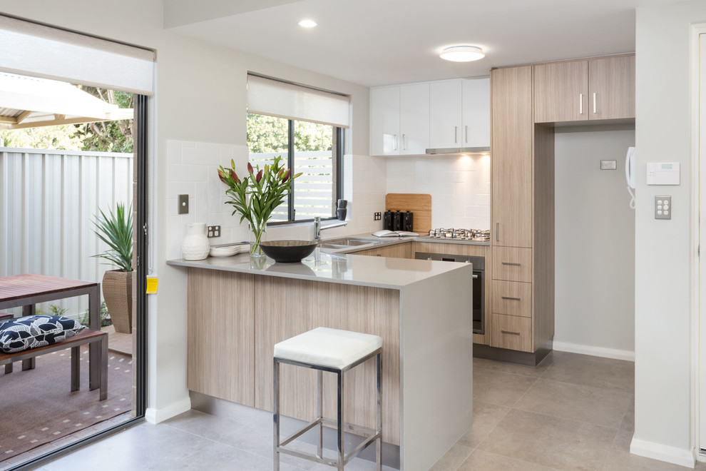 Inspiration for a small contemporary u-shaped eat-in kitchen in Perth with an undermount sink, flat-panel cabinets, medium wood cabinets, quartz benchtops, white splashback, ceramic splashback, stainless steel appliances and porcelain floors.