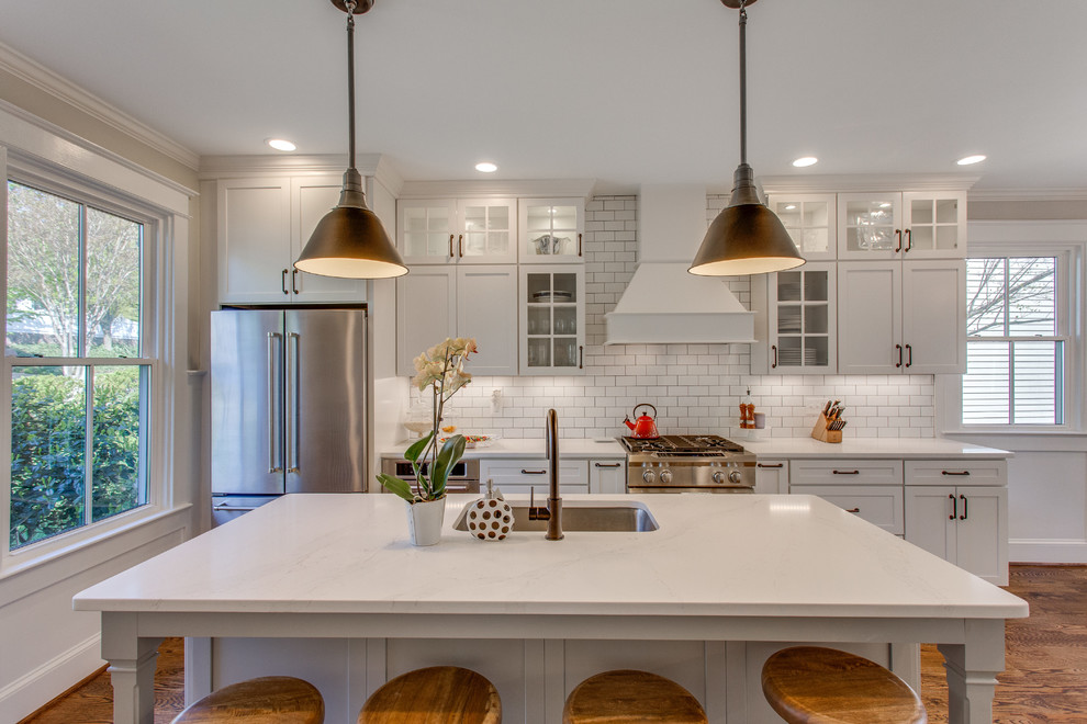 Inspiration for a large arts and crafts single-wall eat-in kitchen in DC Metro with an undermount sink, shaker cabinets, white cabinets, quartz benchtops, white splashback, ceramic splashback, stainless steel appliances, medium hardwood floors, with island, brown floor and white benchtop.