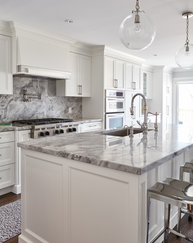 Mid-sized transitional single-wall medium tone wood floor open concept kitchen photo in Toronto with an undermount sink, beaded inset cabinets, white cabinets, marble countertops, gray backsplash, stone slab backsplash, stainless steel appliances and an island