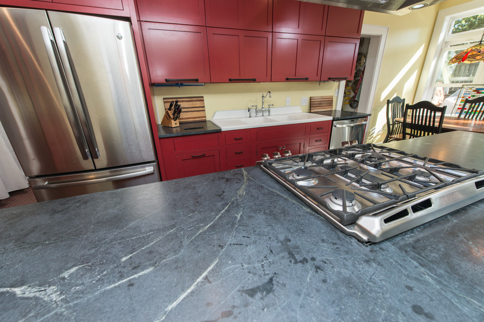 Mid-sized trendy galley dark wood floor and brown floor eat-in kitchen photo with a double-bowl sink, raised-panel cabinets, red cabinets, soapstone countertops, stainless steel appliances and an island