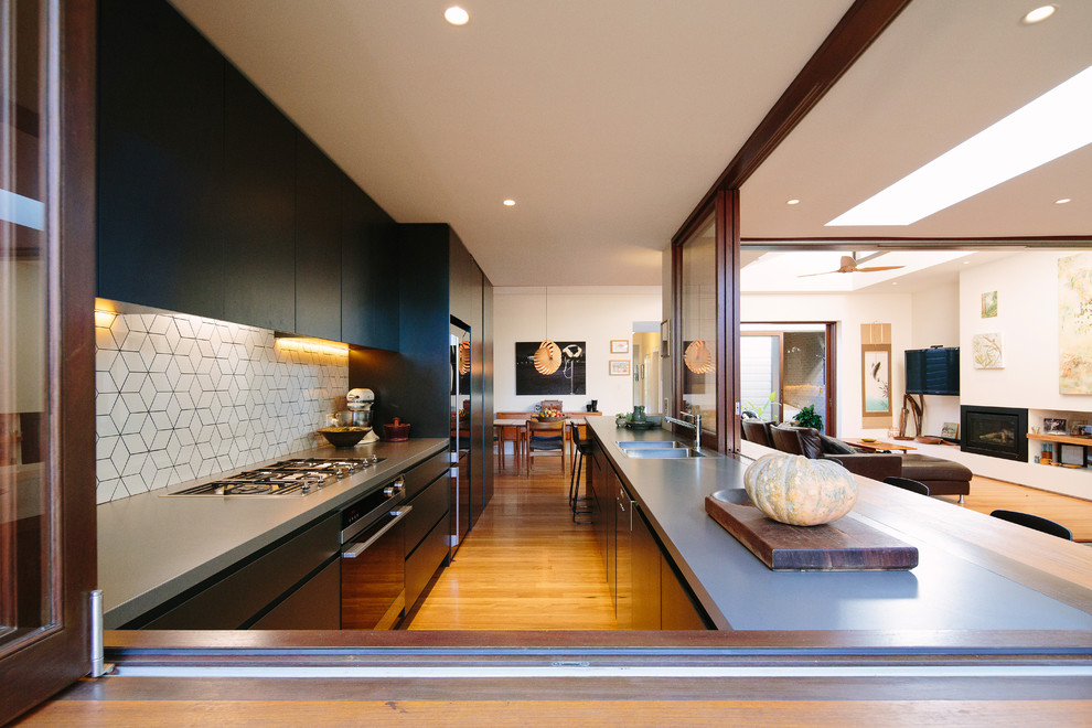 Photo of a mid-sized contemporary u-shaped open plan kitchen in Sydney with an integrated sink, flat-panel cabinets, black cabinets, concrete benchtops, white splashback, medium hardwood floors and no island.