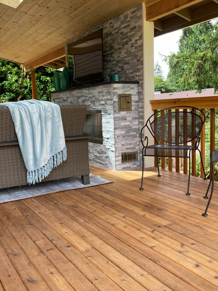 Photo of a large transitional backyard deck with with fireplace, a roof extension and wood railing.