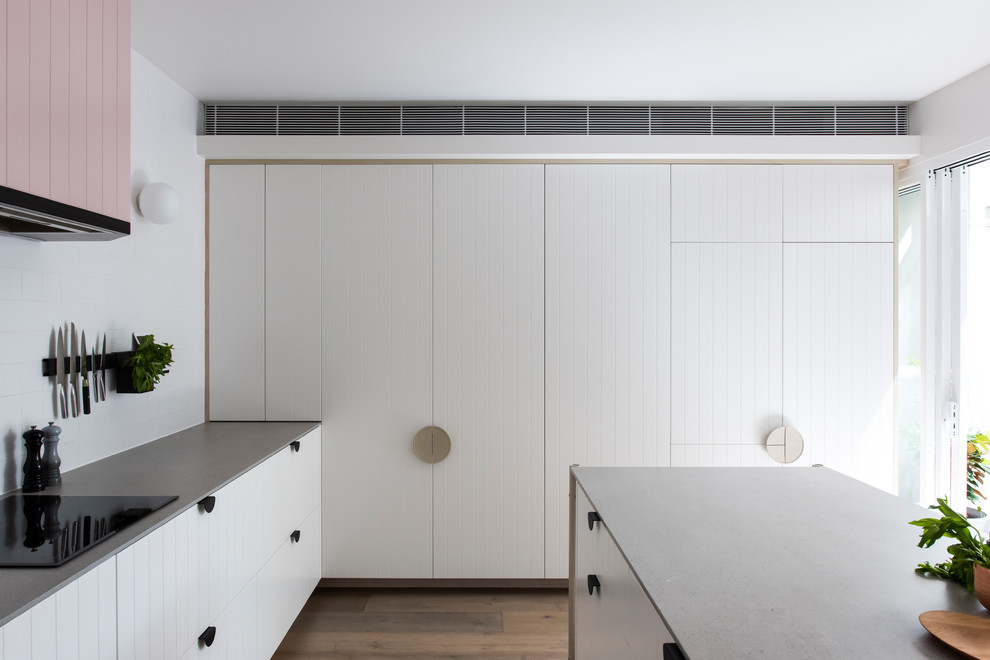 This is an example of a mid-sized contemporary l-shaped open plan kitchen in Sydney with a double-bowl sink, white cabinets, recycled glass benchtops, white splashback, cement tile splashback, black appliances, medium hardwood floors, with island and grey benchtop.