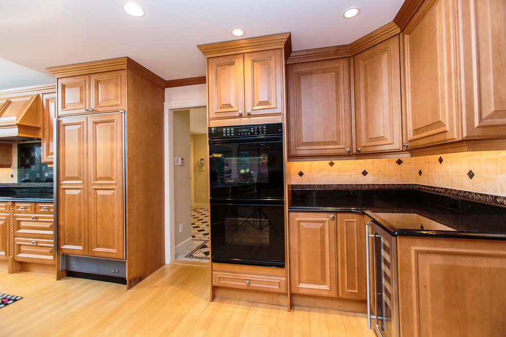 This is an example of a large traditional u-shaped open plan kitchen in Boston with recessed-panel cabinets, medium wood cabinets, black splashback, light hardwood floors and a peninsula.