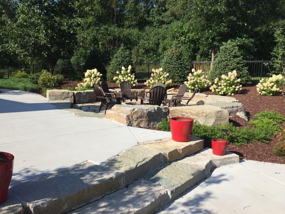 This is an example of a large modern backyard patio in Detroit with a fire feature and natural stone pavers.