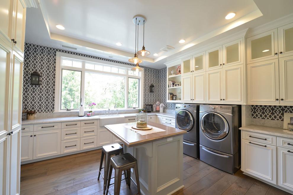 Design ideas for a large traditional l-shaped utility room in Other with a farmhouse sink, recessed-panel cabinets, white cabinets, multi-coloured walls, medium hardwood floors, a side-by-side washer and dryer, quartz benchtops, brown floor and beige benchtop.