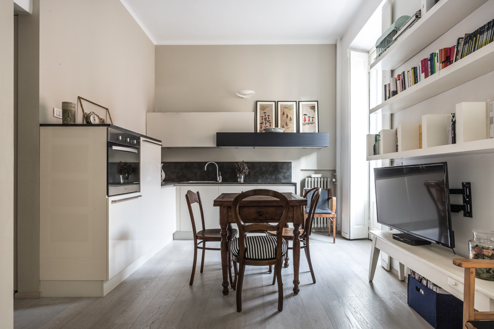 This is an example of a small traditional l-shaped eat-in kitchen in Other with flat-panel cabinets, white cabinets, black splashback, light hardwood floors, no island and beige floor.