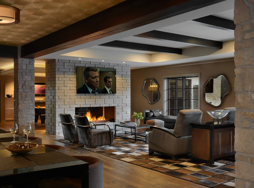 This is an example of a transitional walk-out basement in St Louis with dark hardwood floors, a two-sided fireplace, a stone fireplace surround, exposed beam and wallpaper.