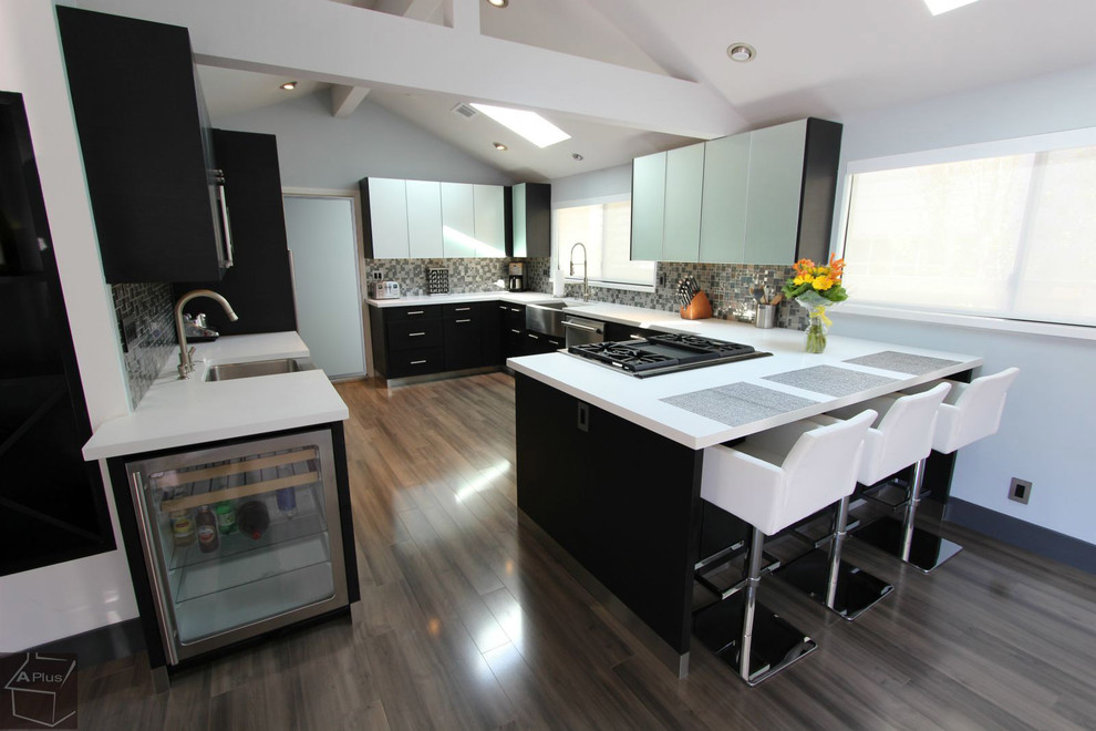 Large minimalist u-shaped medium tone wood floor eat-in kitchen photo in Orange County with a farmhouse sink, flat-panel cabinets, black cabinets, quartz countertops, gray backsplash, porcelain backsplash, stainless steel appliances and a peninsula