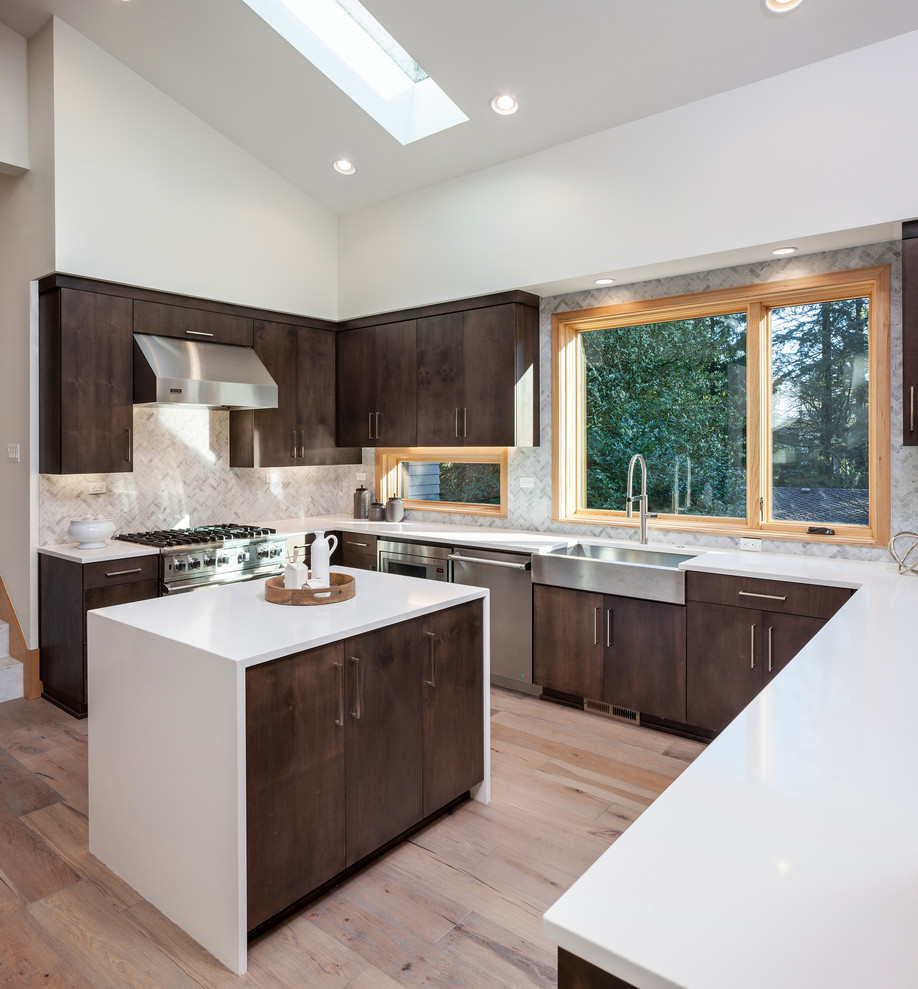 Design ideas for a midcentury u-shaped kitchen in Portland with a farmhouse sink, flat-panel cabinets, dark wood cabinets, window splashback, stainless steel appliances, light hardwood floors, with island, beige floor and white benchtop.