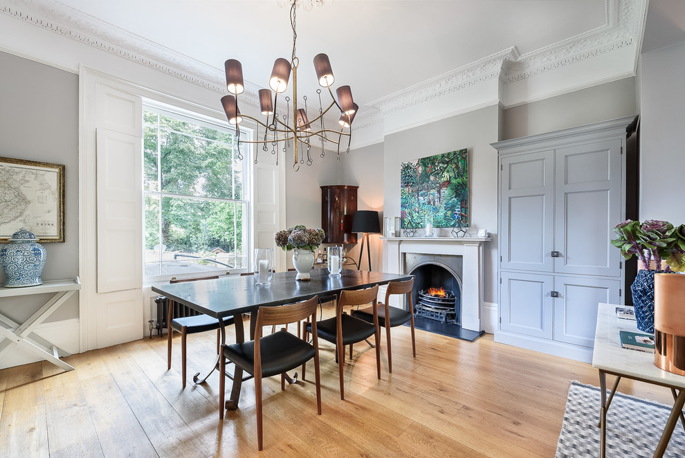 Inspiration for a large transitional open plan dining in London with grey walls, light hardwood floors, a standard fireplace, a stone fireplace surround and yellow floor.
