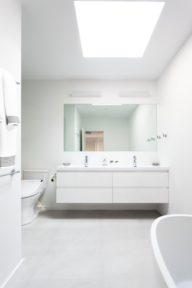 Inspiration for a medium sized modern ensuite bathroom in San Francisco with flat-panel cabinets, white cabinets, a freestanding bath, an alcove shower, a two-piece toilet, white walls, ceramic flooring, a submerged sink, engineered stone worktops, grey floors, a hinged door, white worktops, double sinks and a floating vanity unit.