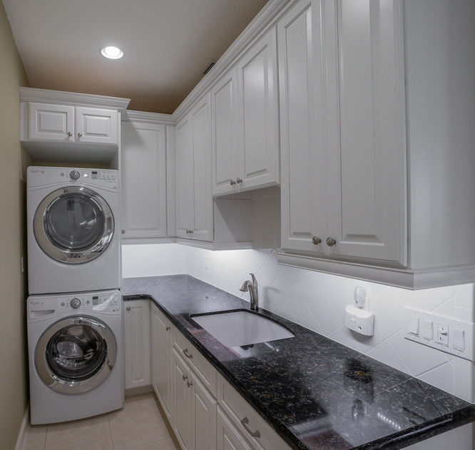 Laundry room - traditional laundry room idea in Miami with an undermount sink, white cabinets, quartz countertops and a stacked washer/dryer