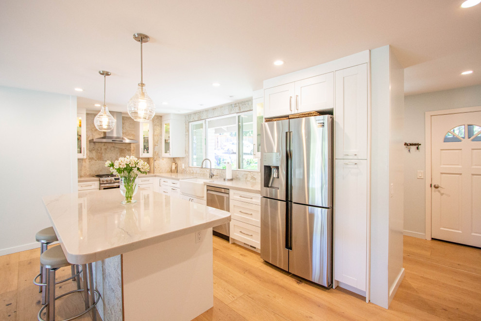 Eat-in kitchen - transitional l-shaped light wood floor and brown floor eat-in kitchen idea with a farmhouse sink, shaker cabinets, white cabinets, quartz countertops, porcelain backsplash, stainless steel appliances and an island
