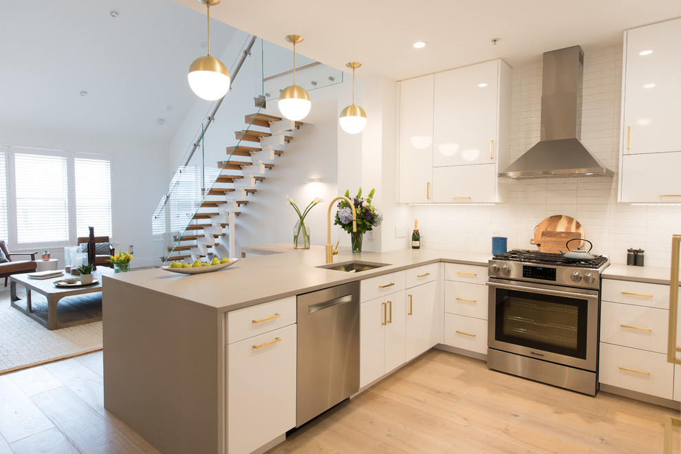 This is an example of a mid-sized contemporary kitchen in New York with an undermount sink, flat-panel cabinets, white cabinets, quartz benchtops, white splashback, ceramic splashback, stainless steel appliances, laminate floors and brown floor.
