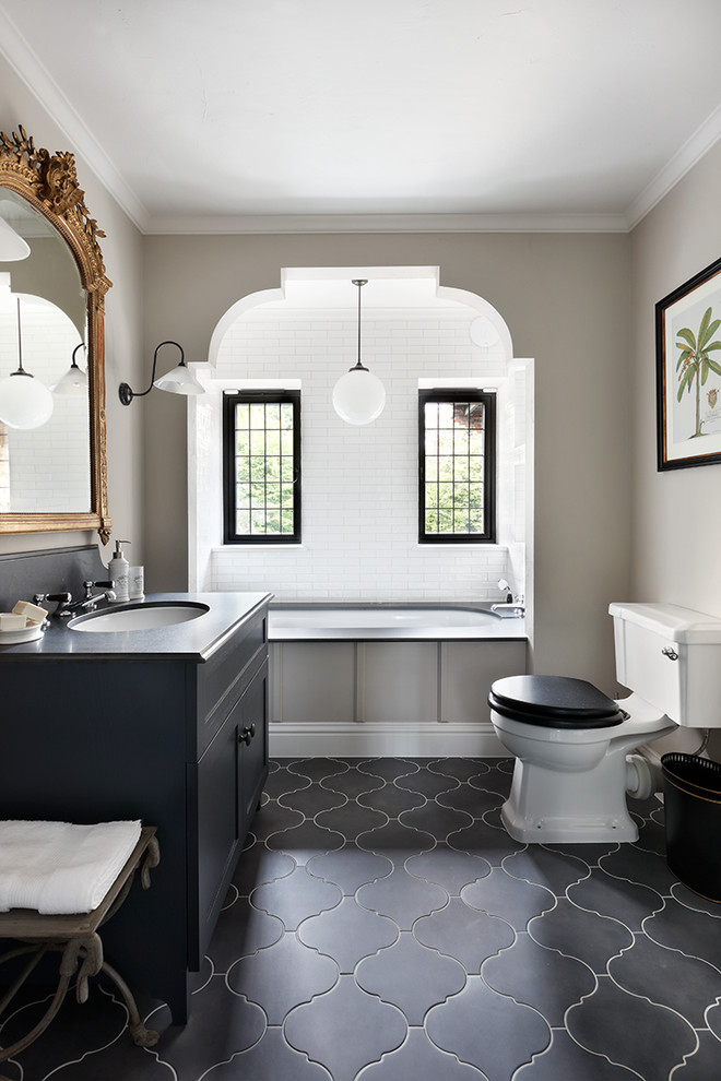 Design ideas for a traditional bathroom in London with shaker cabinets, black cabinets, an alcove tub, a two-piece toilet, beige walls, an undermount sink and black and white tile.