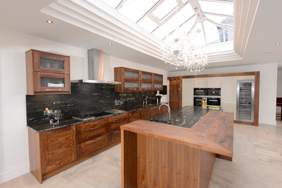Photo of a contemporary open plan kitchen in Manchester with a drop-in sink, shaker cabinets, medium wood cabinets, granite benchtops, black splashback, stainless steel appliances, travertine floors and with island.