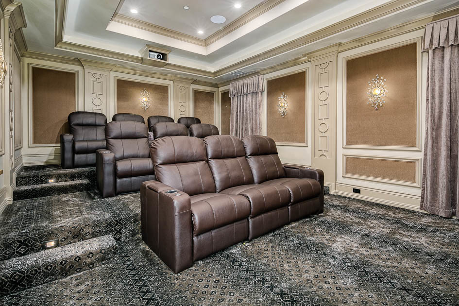 This is an example of a large traditional enclosed home theatre in Los Angeles with brown walls, carpet, a projector screen and black floor.