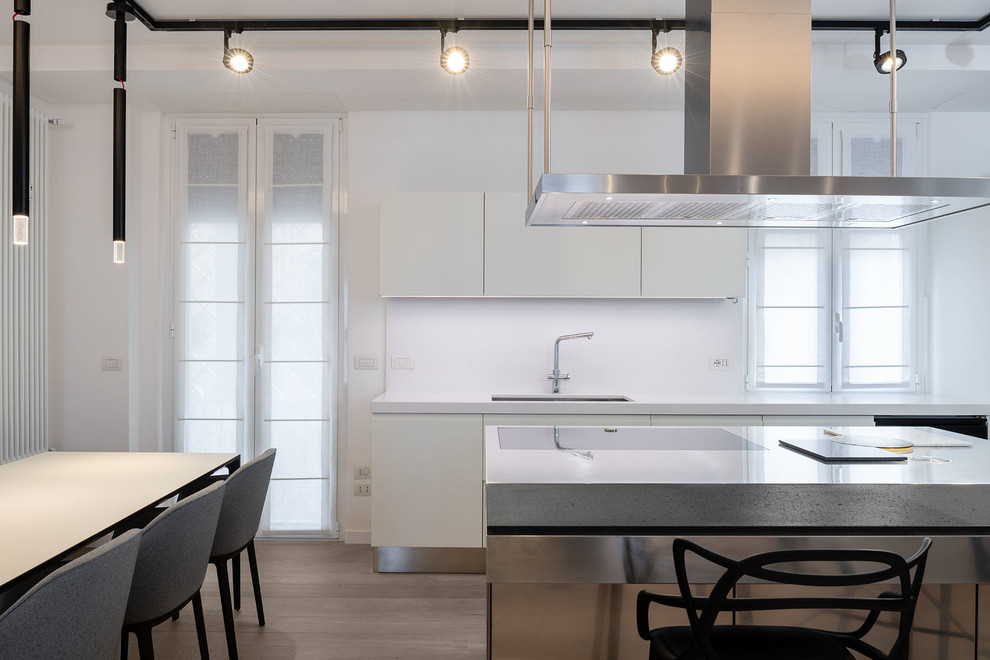 Inspiration for a large contemporary l-shaped eat-in kitchen in Rome with an undermount sink, flat-panel cabinets, white cabinets, solid surface benchtops, white splashback, light hardwood floors, with island, grey floor and white benchtop.